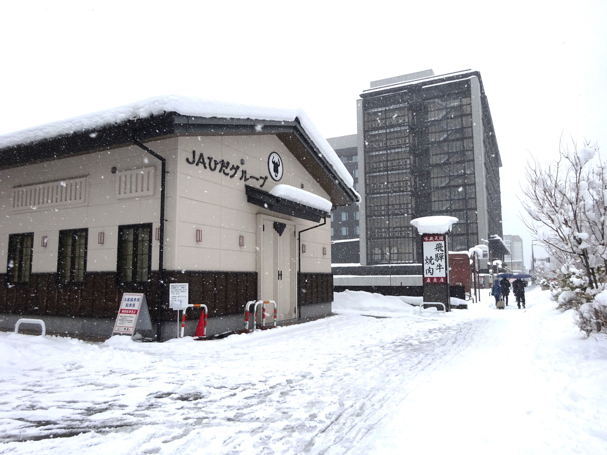 ⑤「味蔵天国」前の歩道で立ち止まり、高山駅方面に振り返って見ると、こんな様子です。建物の「JAひだグループ」と看板が目印。奥に見える高層の建物は「東急ステイ飛騨高山 結の湯」です。